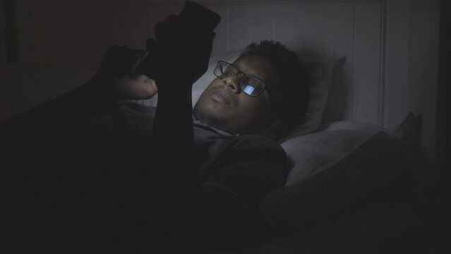 young man using smart phone at night on bed 