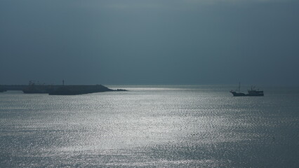 The peaceful sea view with the fishing boat sailing on it in the cloudy day