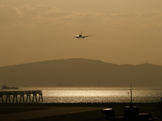 陽が反射する海を背景に着陸してくる飛行機