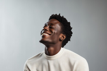Obraz premium Closeup of young black man with head tilted up smiling with eyes closed on a white background. Minimalist image. Harmonies of luminous colors. Sincere and natural photography. Copy space.