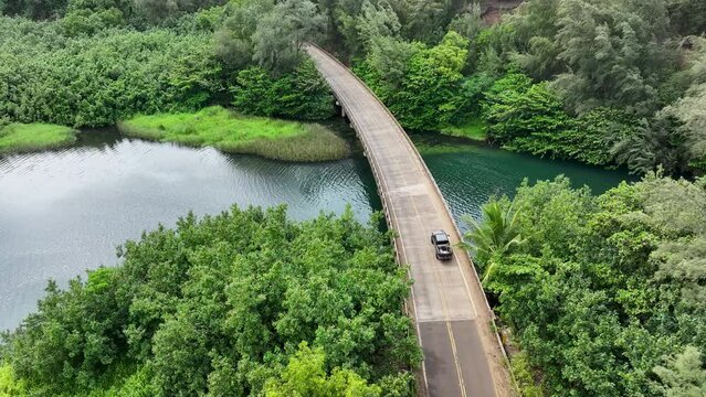 Aerial coastal river bridge traffic Kauai Hawaii. Coastal road around the beaches and plantations of the island. Rivers enter lagoons and Pacific Ocean. Economy is tourism based.