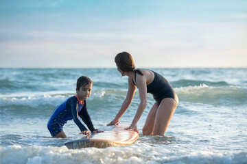 Little boy and mother helping holding surfboard into the sea  and waiting for big wave, mother teaches her son to  surfing on wave, lifestyle activities, water sports