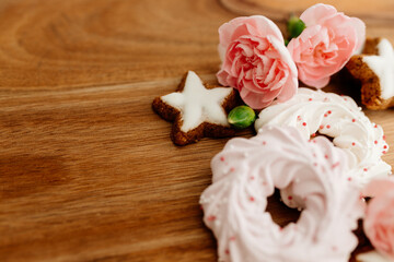 Obraz na płótnie Canvas Gingerbread cookies in the shape of stars, pink merengue cookies and pink roses on a wooden brown natural table. Christmas and Winter card. Delicious pastries close-up. Valentine’s Day background