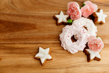 Gingerbread cookies in the shape of stars, pink merengue cookies and pink roses on a wooden brown natural table. Christmas and Winter card. Delicious pastries close-up. Valentine’s Day background