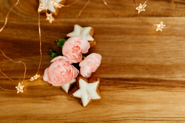Gingerbread cookies in the shape of stars, merengue cookies and pink roses on a wooden table against a background of bokeh of New Year’s lights. Christmas background. Winter card. Delicious pastries