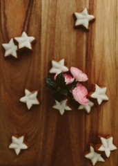 Obraz na płótnie Canvas Gingerbread cookies in the shape of stars and pink roses on a wooden table. Christmas background. Winter card. Delicious pastries