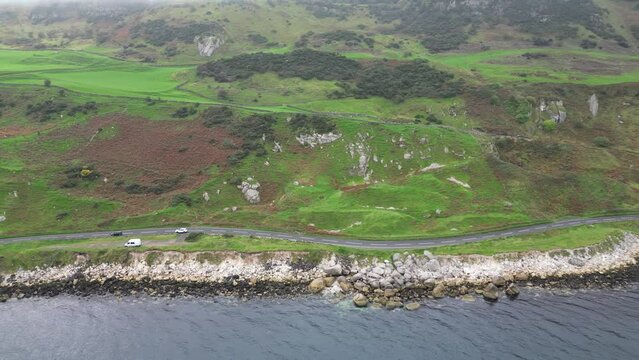 Aerial panning view over the idyllic rocky coast road right on the sea with moving cars during an adventurous trip near glenarm town in Northern Ireland