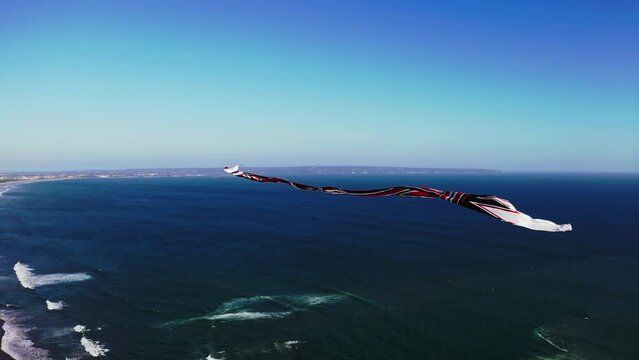 Traditional balinese kite with long flowing tail flying high above sea.