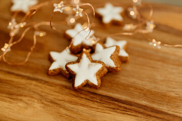 Fototapeta na wymiar Gingerbread cookies in the shape of stars on a wooden brown natural table against a background of bokeh of New Year's golden lights. Christmas background. Winter card. Delicious pastries close-up