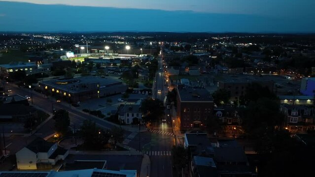 American city at dusk. Aerial shot of urban street with stadium lighting at minor league baseball game in background during night game.