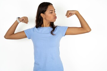 Beautiful girl wearing blue T-shirt showing arms muscles smiling proud. Fitness concept.