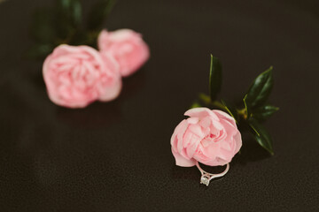 Delicate pink roses and diamond engagement ring on a black background close up. Pink carnations. Beautiful flowers, a gift for February 14, Valentine's Day, Mother's Day. Place for text. Mock up.