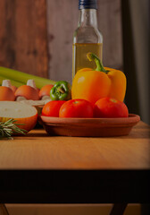 Kitchen table with assorted vegetables,herbs and fresh eggs and olive oil on it.