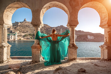 Woman dress sea columns. Rear view of a happy blonde woman in a long mint dress posing against the backdrop of the sea in an old building with columns.