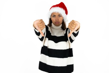 Beautiful woman wearing christmas hat being upset showing thumb down with two hands. Dislike...