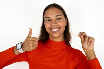 Young beautiful woman holding an invisible braces aligner and rising thumb up, recommending this new treatment. Dental healthcare concept.