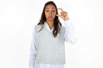 Young beautiful woman purses lip and gestures with hand, shows something very little.