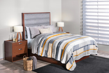 Contemporary bedroom showcasing a wooden bed, featuring a gray fabric headboard, striped multicolor...
