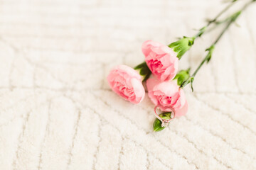Delicate pink roses and diamond engagement ring on off white fluffy carpet close up. Pink carnations. Beautiful flowers, a gift for February 14, Valentine's Day, Mother's Day. Place for text. Mock up.