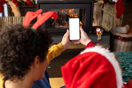 Diverse gay male couple wearing christmas hats and having smartphone video call at home, copy space