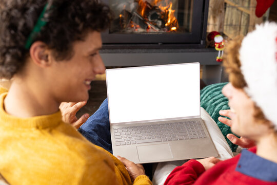 Diverse gay male couple wearing christmas hats and having laptop video call at home, copy space