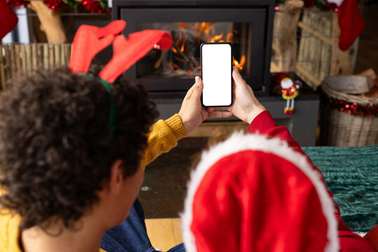Diverse gay male couple wearing christmas hats and having smartphone video call at home, copy space
