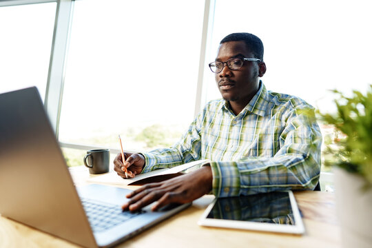 Serious concentrated african man studying or working with laptop indoors