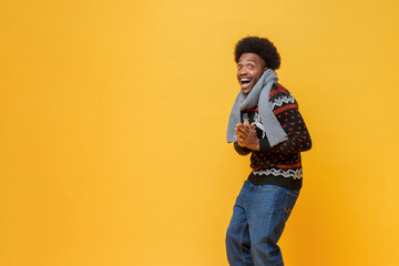 Happy young African-American man in Christmas sweater and scarf expressing surprise feeling in isolated yellow background with copy space studio shot - obrazy, fototapety, plakaty