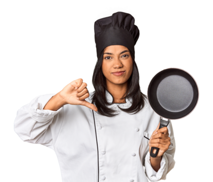 Young Filipina chef holding pan by handle showing a dislike gesture, thumbs down. Disagreement concept.