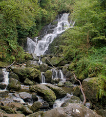A long-exposure view of the water pouring through a thick green forest and into the rocky and steep Torc Waterfall. Ring of Kerry, County Kerry, Ireland