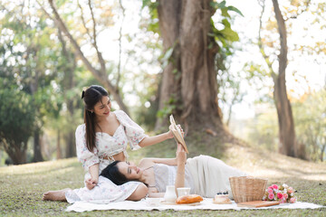 Two beautiful LGBT young women in casual clothes and summer hats Carefree woman having a picnic outside Positive model sitting on the grass eat fruit and cheese Take a selfie. LGBT concept