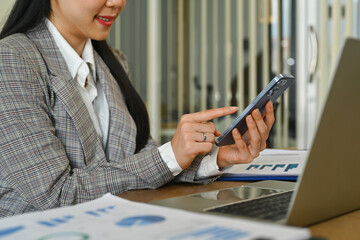 Smiling female manager typing massage, communicating online on mobile phone while sitting at workplace