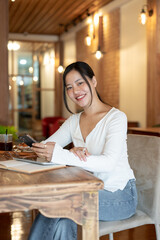 A beautiful Asian woman sits at a table in a beautiful coffee shop with a smartphone in her hand.