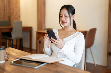 An attractive Asian woman is using her smartphone while relaxing in a coffee shop.