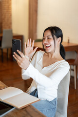 A cheerful woman enjoys talking with her friend through a video call on her phone in a coffee shop.