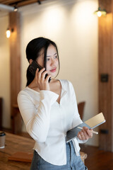A beautiful Asian woman is calling or talking with someone on her phone while standing in a cafe.