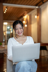 A beautiful and happy Asian woman is using her laptop while sitting in a coffee shop.