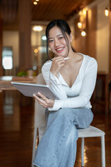 A beautiful and happy Asian woman is using her digital tablet while sitting in a coffee shop.