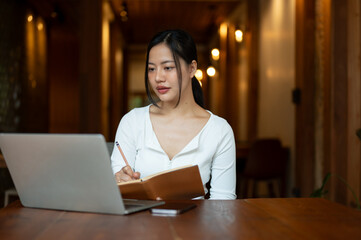 A beautiful Asian woman is studying online or working remotely at a coffee shop.