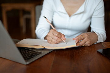Cropped image of a woman writing some ideas down in her book, working remotely at a coffee shop.
