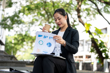 A busy businesswoman is sipping coffee and reviewing business documents while sitting on the stairs.