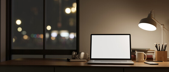 A white-screen laptop mockup on a table against the window and wall in a modern dark room at night. - obrazy, fototapety, plakaty