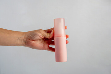 Cosmetic pink bottle. Womens cosmetic accessory and hand for makeup on grey background.
