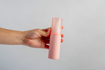 Cosmetic pink bottle. Womens cosmetic accessory and hand for makeup on grey background.