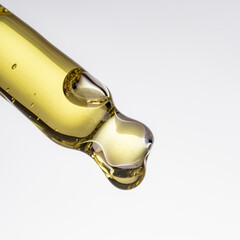 Yellow essential serum oil dripping from gold dropper isolated on white background.