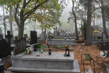 Warsaw, Poland - October 24, 2023: Graves in the cemetery on a cloudy, foggy day. Weather for All Saints' Day. Candles and flowers on graves.