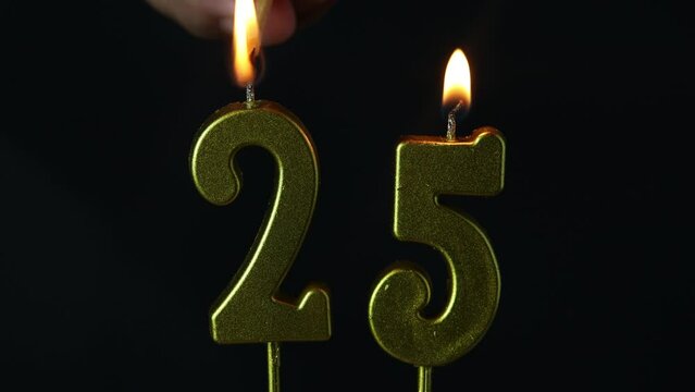 close up on the gold number twenty-fifth candle on a dark background.
 - Powered by Adobe