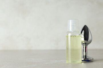 Lubricant and metal butt plug, on a gray background.