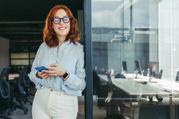 Professional businesswoman smiling and using her smartphone in a tech office