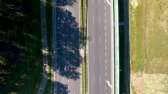 Top-down aerial shot of a highway with vehicles, flanked by greenery and shadows.